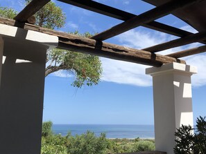 A covered outdoor area with a view of the sea, wooden beams, and white pillars.