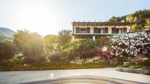 Un edificio moderno con balcón, rodeado de abundante vegetación y plantas en flor.
