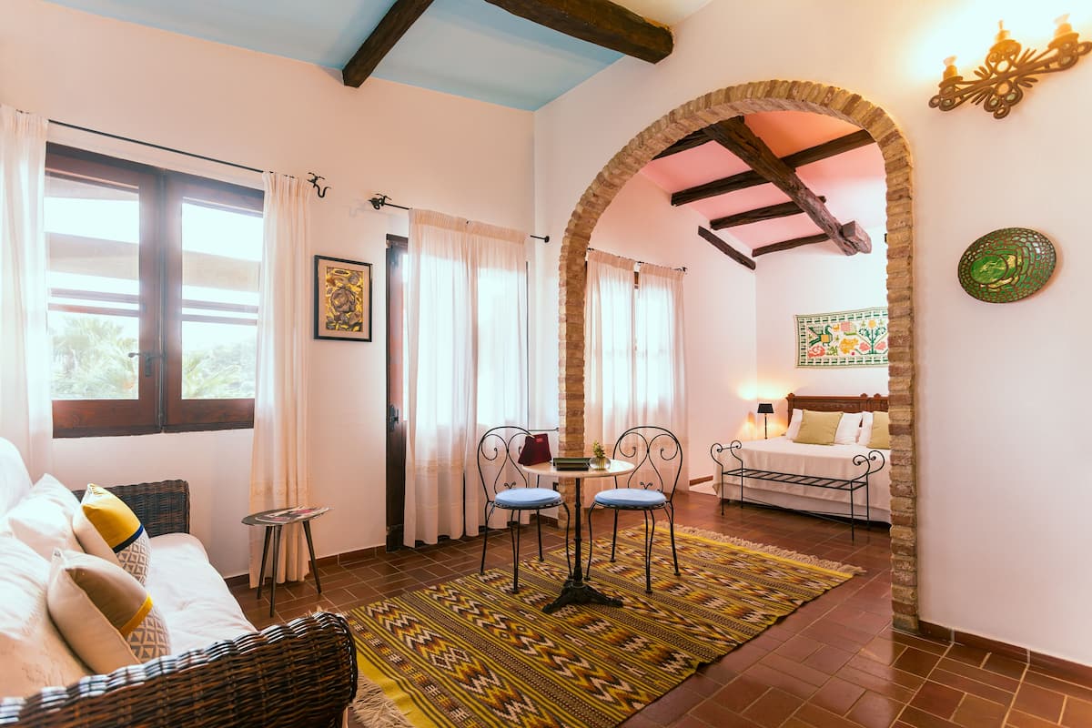A cozy room with a bed, a dining area with a table and chairs, and a view through an archway to another room with a bed.