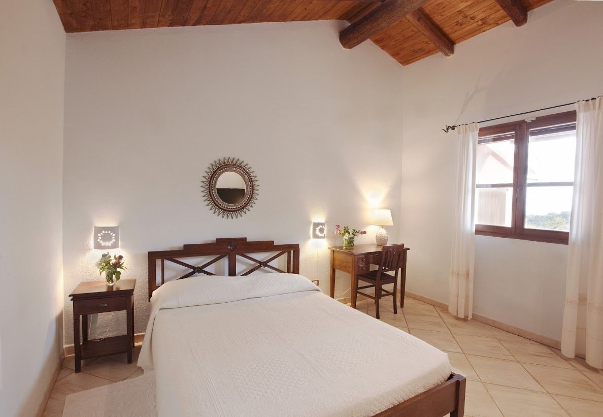 A bedroom with a wooden bed, two bedside tables with lamps, a mirror, and a window with curtains.