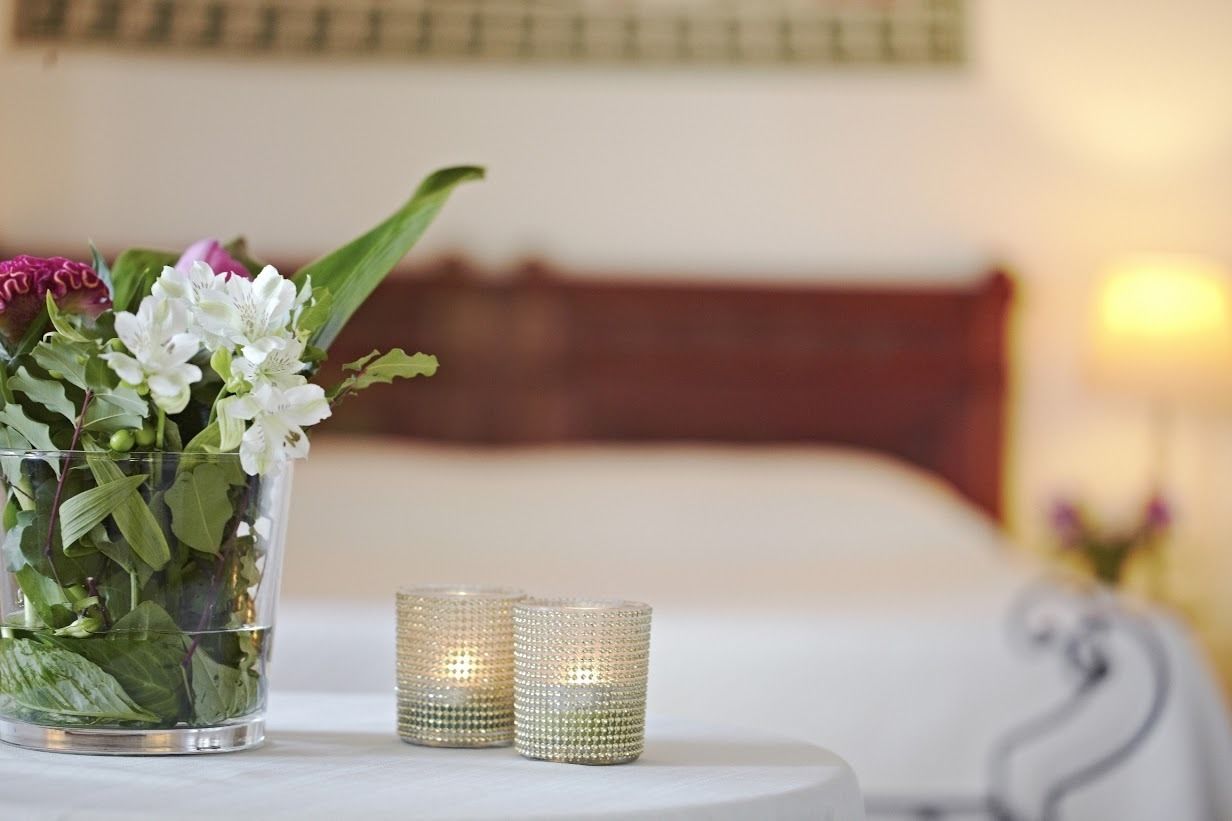 Una camera d'albergo con un letto, un comodino con un vaso di fiori e due candele accese.