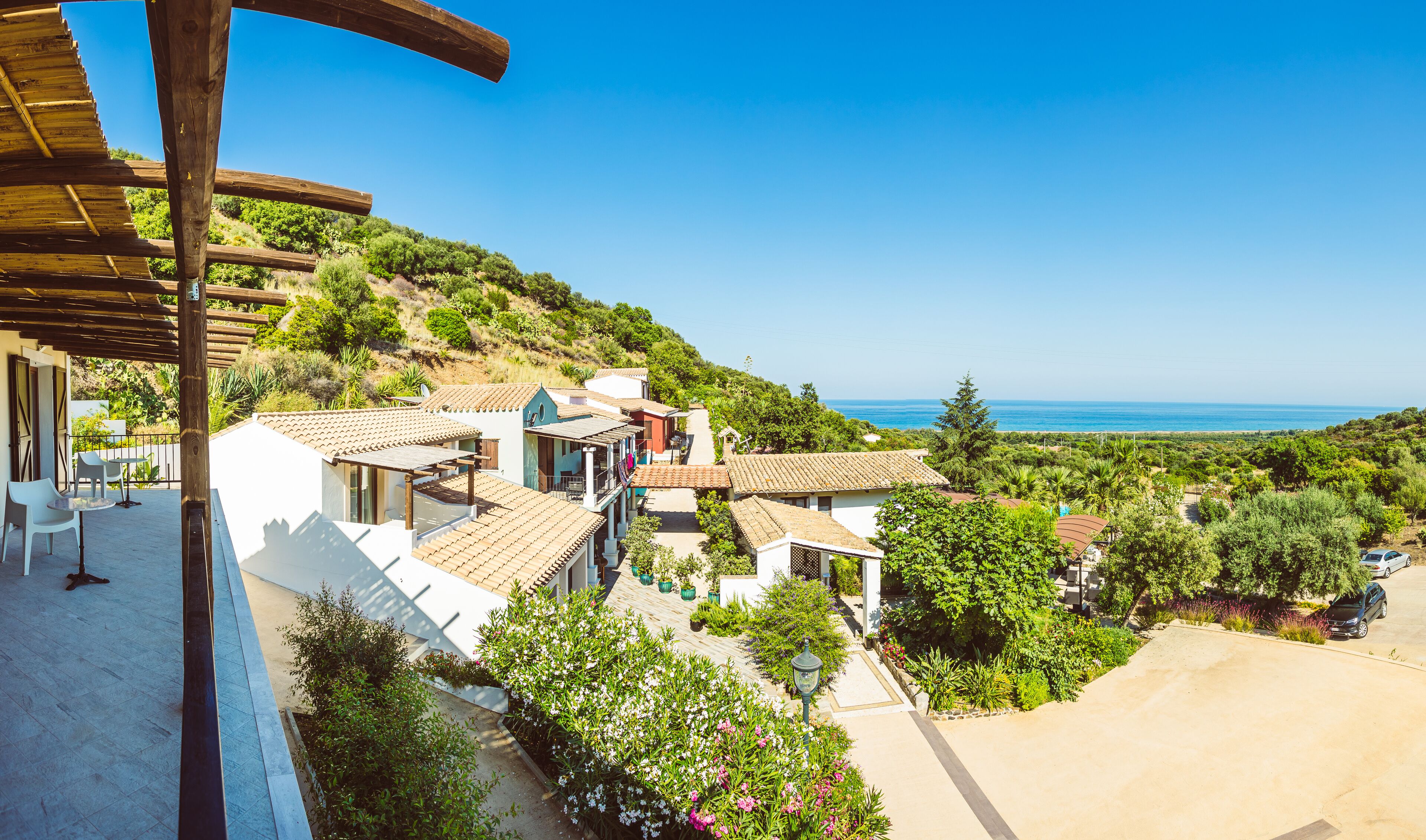 A coastal village with terracotta-roofed houses, a paved walkway, and a view of the sea.