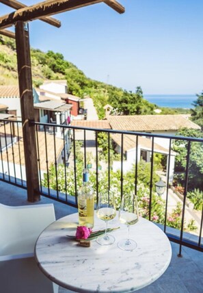 A round table with a bottle and two glasses on a balcony overlooking a coastal view. - Relais Rio Molas (Muravera)