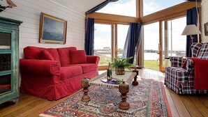 A cozy living room with a red sofa, plaid armchair, and a large window offering a view of the sea. - Hotel Kullaberg (Molle)