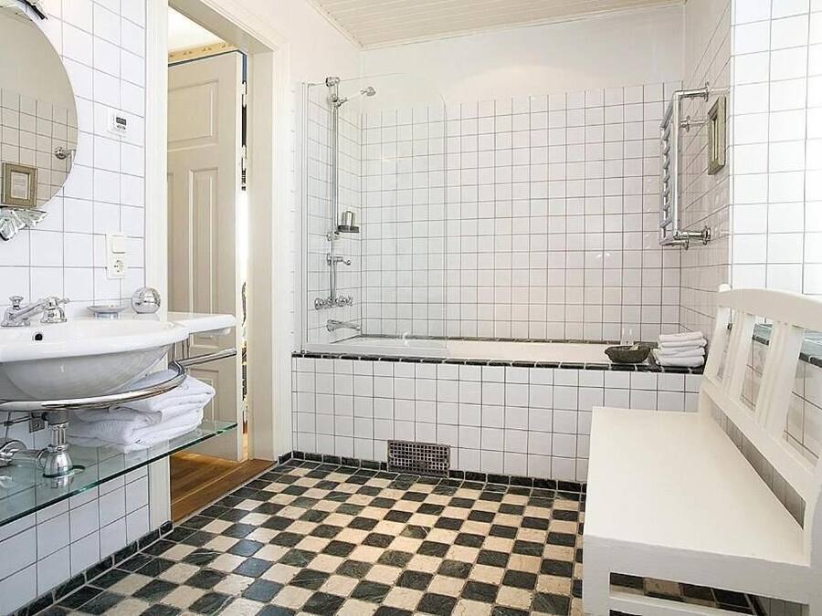 Baño con piso a cuadros, un lavamanos blanco, una repisa de vidrio y zona de ducha.