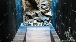 A narrow, tiled shower area with a rock wall backdrop and a drain in the center. - Hotel Kullaberg (Molle)