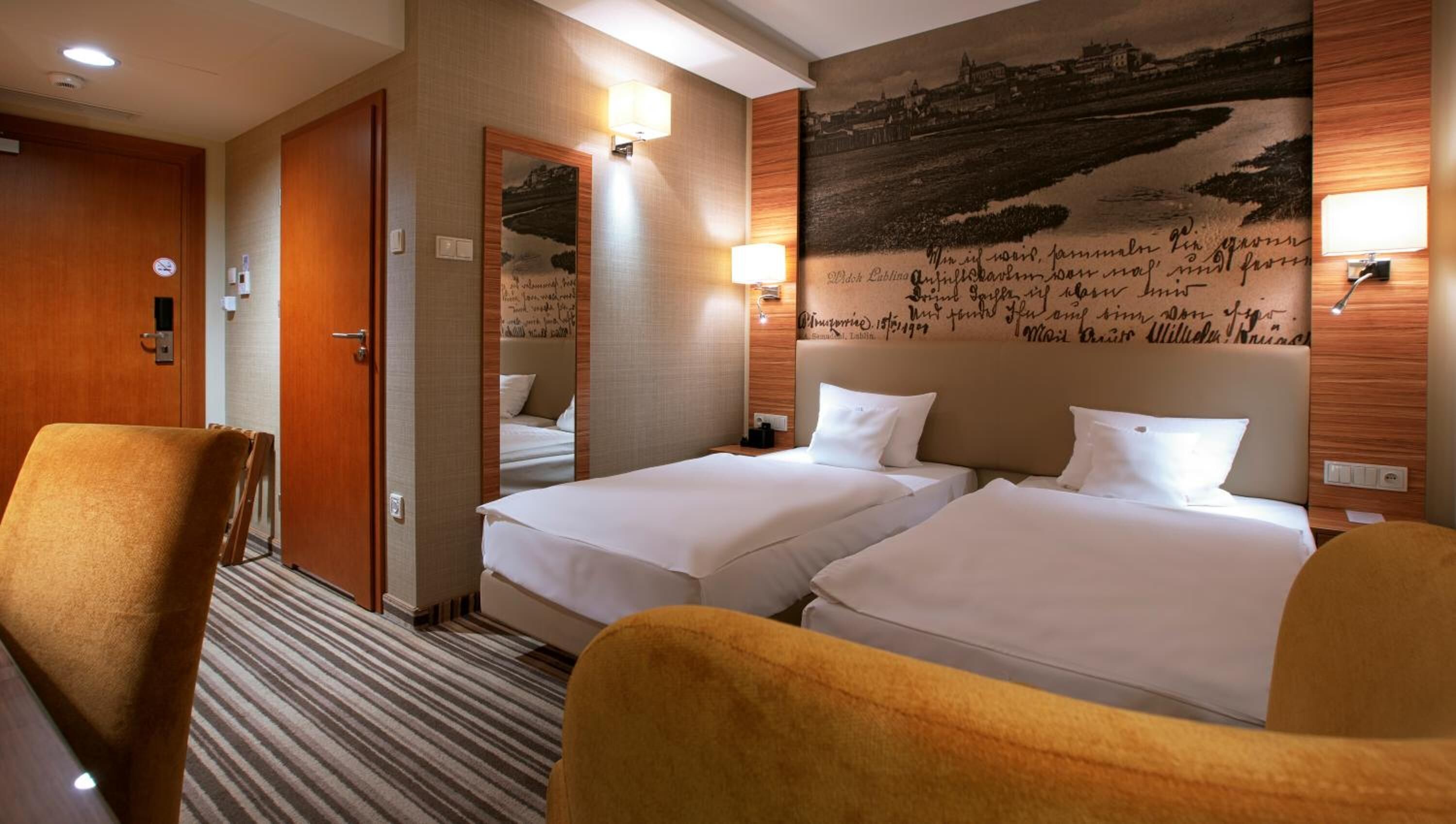 A hotel room with two beds, a wooden door, a mirror, and a wall with a scenic mural.
