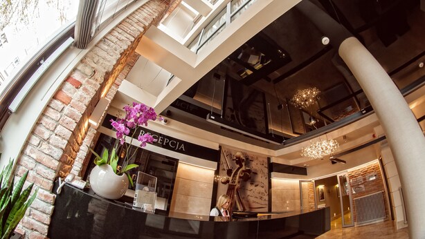 Un intérieur moderne avec un comptoir d’accueil, un mur en briques et une balustrade en verre donnant sur un niveau inférieur.