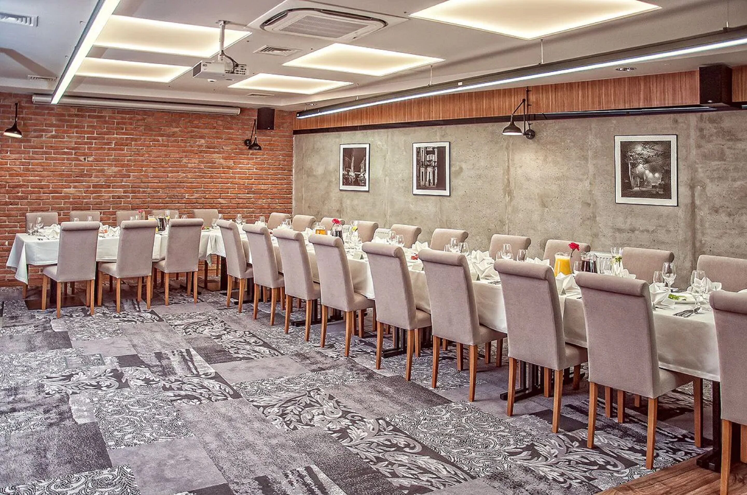 Un salón de conferencias con una larga mesa dispuesta para una reunión, equipado con sillas y mesas, y una alfombra estampada.