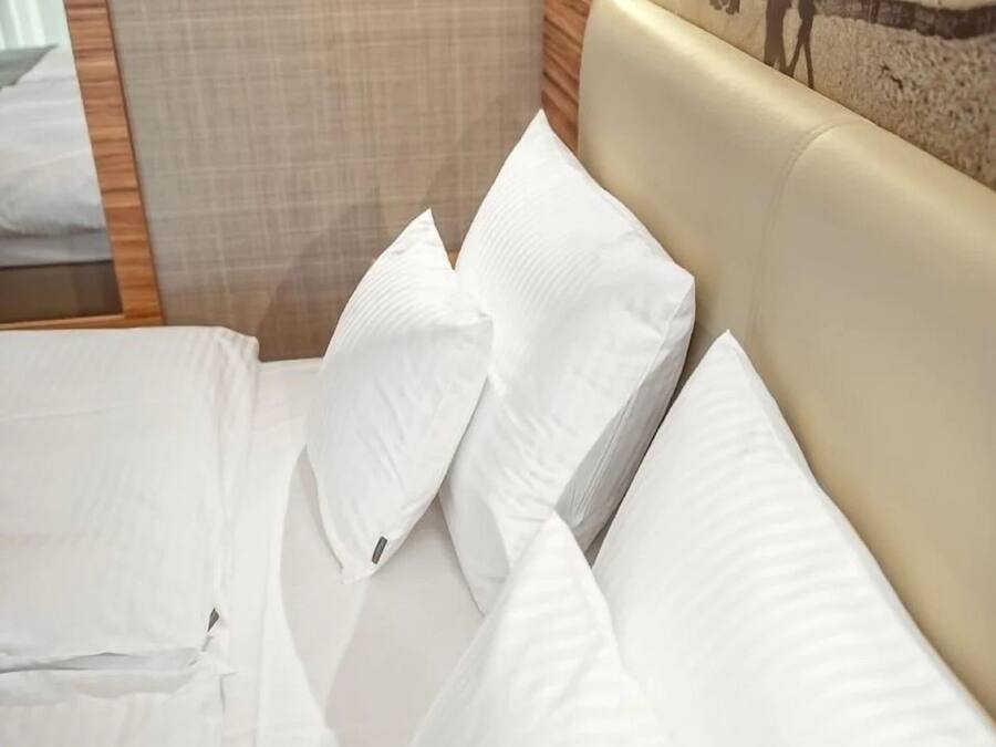 A hotel room with a bed, white linens, a wall-mounted light, and a framed picture on the wall.