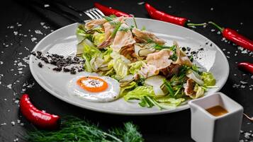 A plate of food with a fried egg, salad, and bread on a dark surface with scattered red chili peppers and a small dish of sauce.