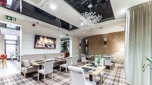 Un restaurant moderne avec un sol à carreaux, des chaises blanches et une fresque représentant une cheminée.