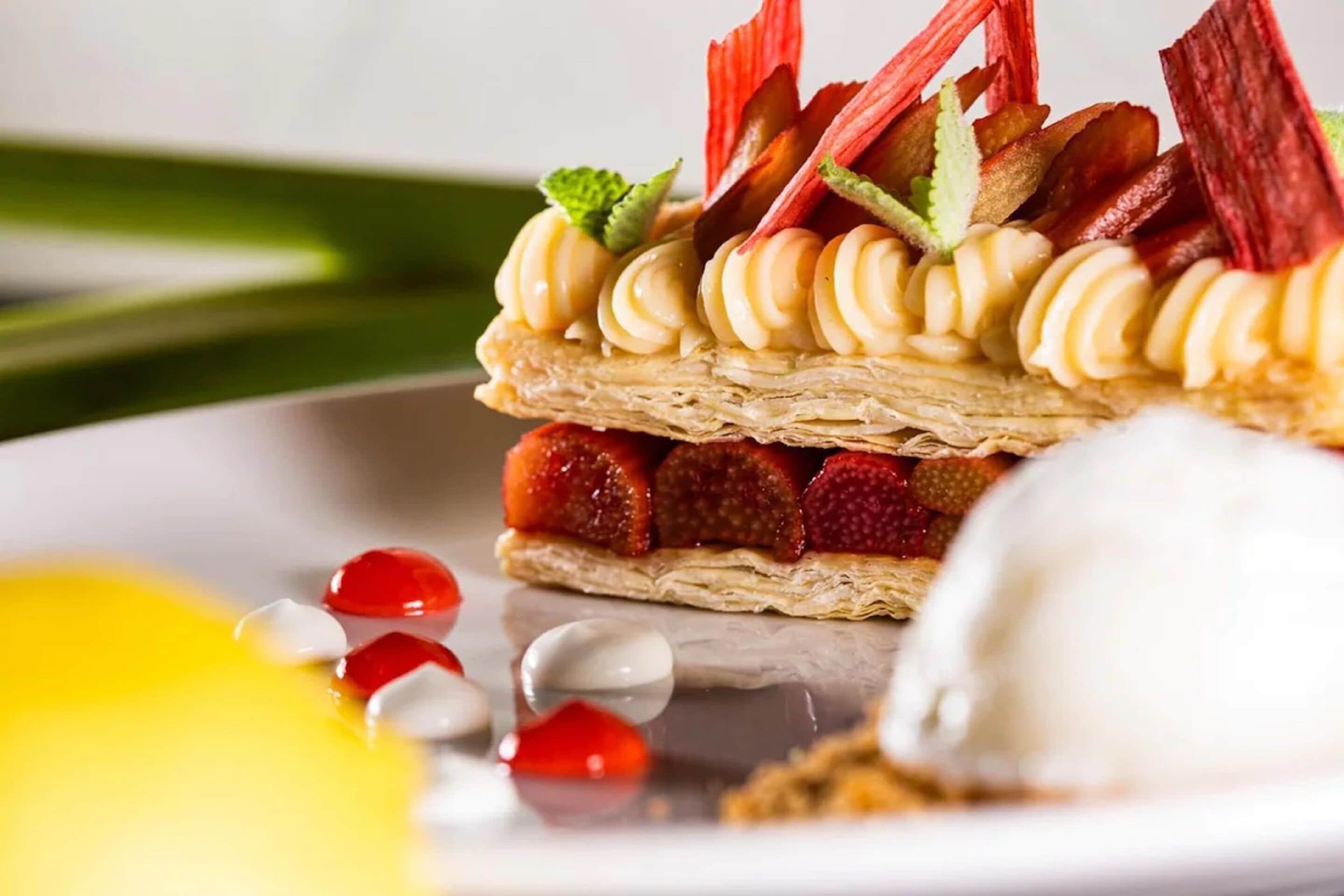 A dessert with cream swirls, strawberries, and red leaf garnishes on a plate.