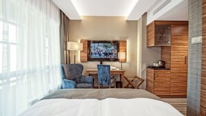 Une chambre d’hôtel avec un grand lit, un bureau avec une chaise, un téléviseur fixé au mur et une armoire.