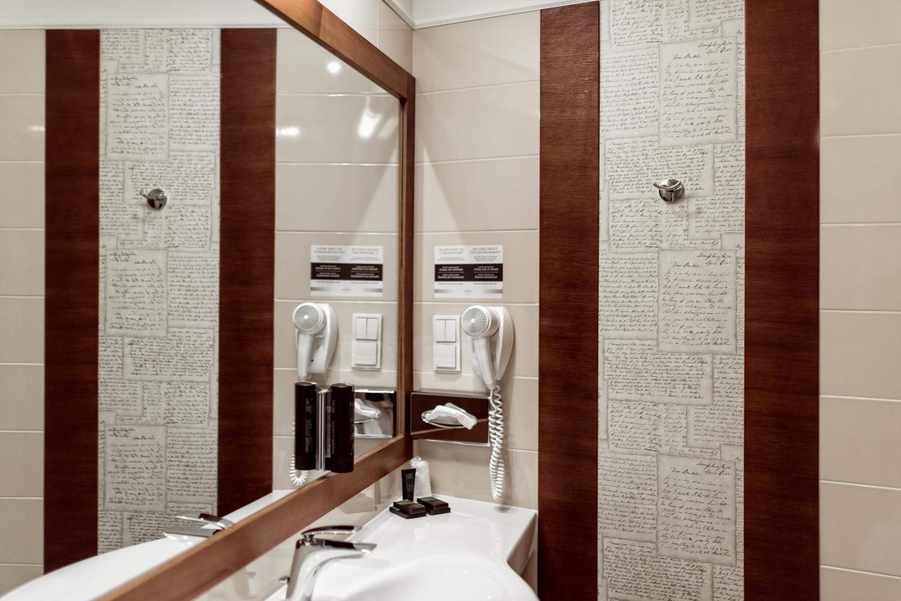 A hotel bathroom with a mirror, a sink, a hairdryer, and a telephone.