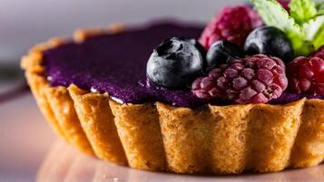 Una tarta con corteza dorada y relleno morado, cubierta con arándanos, frambuesas y una hoja de menta.