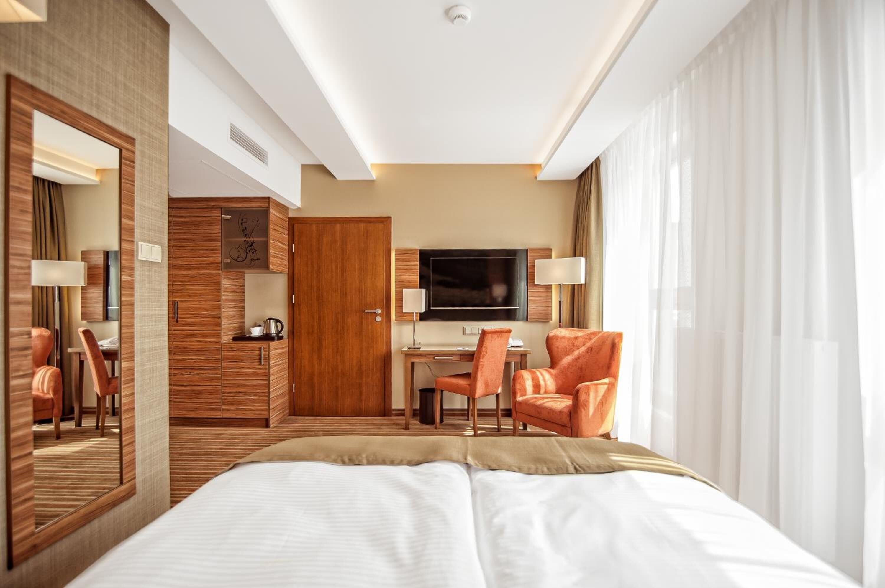 A hotel room with a bed, a desk, a TV, and a seating area.