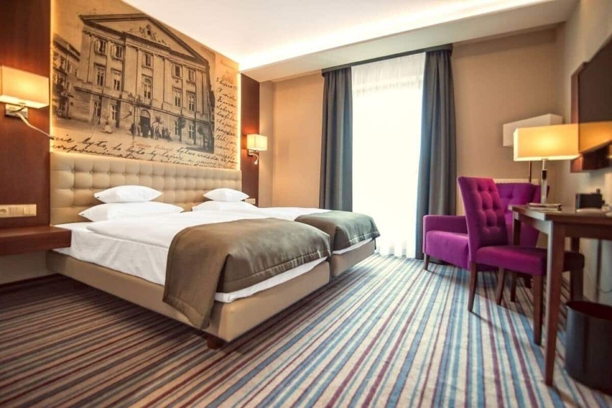 A hotel room with a large bed, a desk, a chair, and a wall with a historical mural.