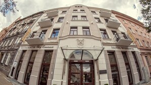 Un hôtel à la façade classique, avec une entrée centrale ornée de blasons et des balcons à chaque étage.
