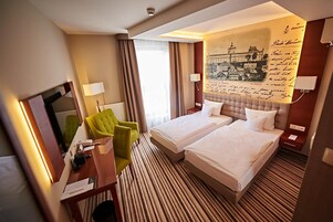 Habitación de hotel con dos camas, un escritorio, una silla y un mural grande en la pared.