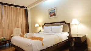 Una habitación de hotel con una cama grande, dos lámparas de noche, una silla, un escritorio con lámpara y un cuadro en la pared.