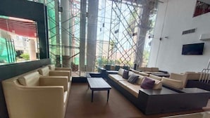 Un área de estar moderna con sofás, sillones, una mesita de centro y una pantalla de televisión en la pared.