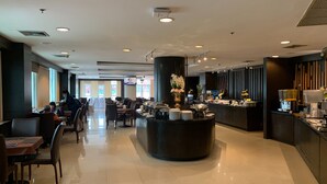 Un moderno vestíbulo de hotel con una barra redonda central, zona de comedor con mesas y sillas, y una recepción.