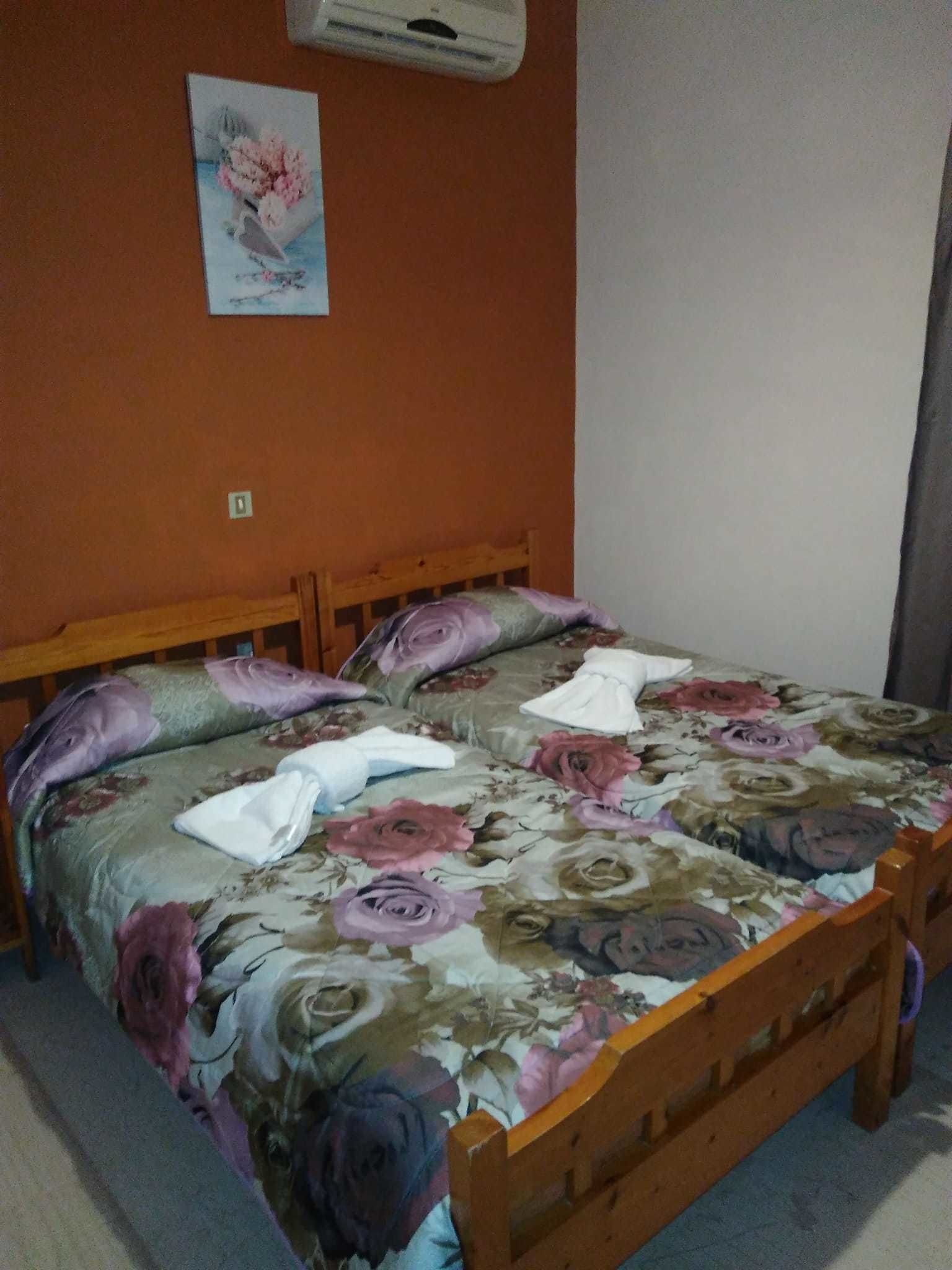 Una cama con cubrecama floral, cabecera de madera y aire acondicionado instalado en la pared.
