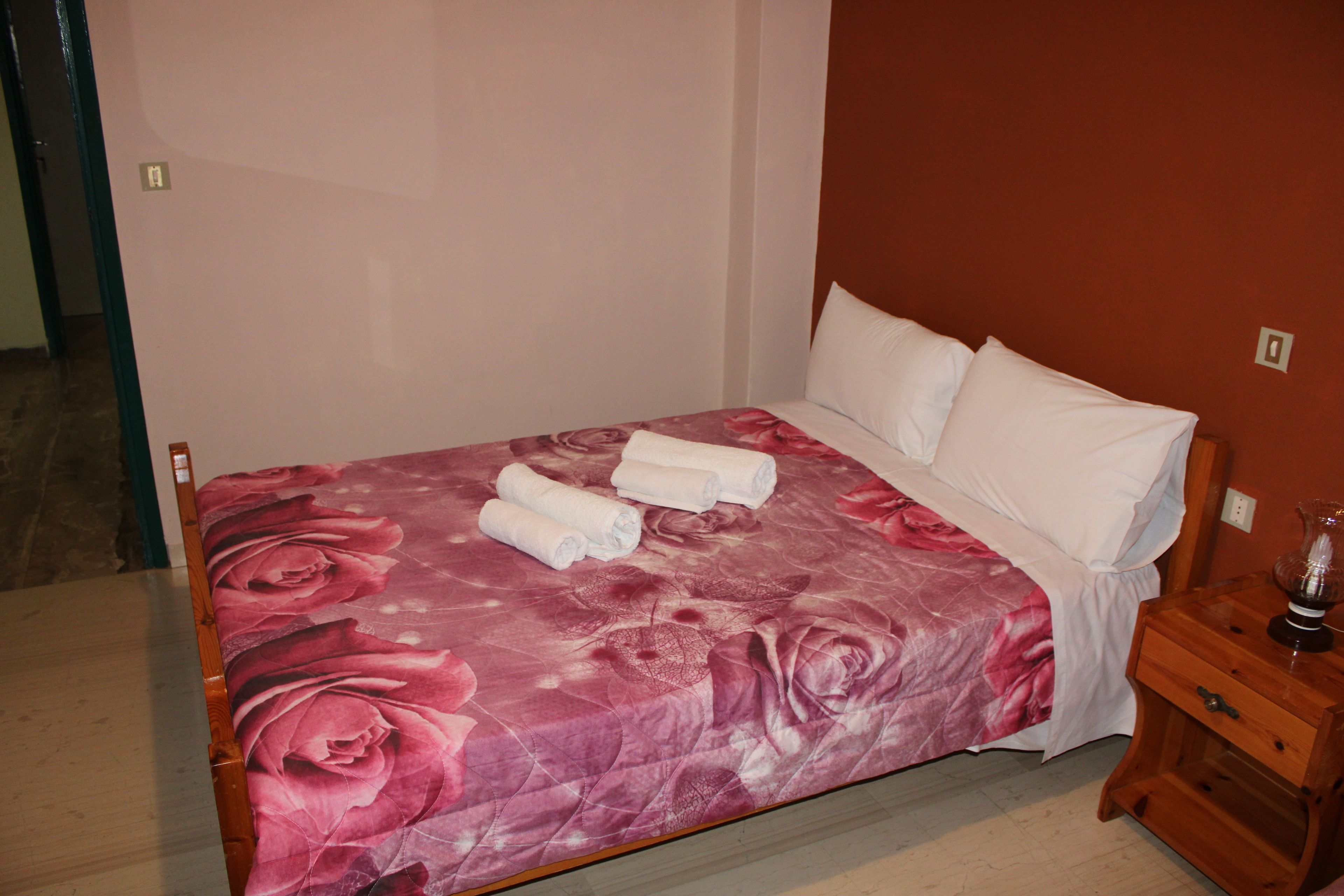Una cama con una colcha floral, almohadas blancas y toallas enrolladas al lado.