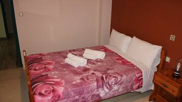 Una cama con una colcha floral, almohadas blancas y toallas enrolladas al lado.