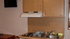 Una cocina compacta con armarios de madera, un refrigerador pequeño, un lavamanos y una estufa.
