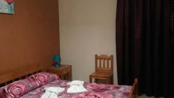 Un dormitorio con una cama, una silla de madera, una mesita de noche, un aire acondicionado y una televisión.