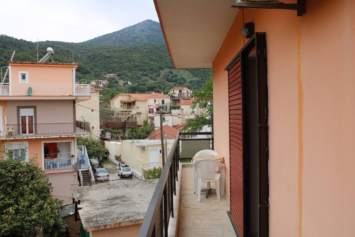 Un balcón con vistas a una zona residencial, una silla blanca y una puerta roja.