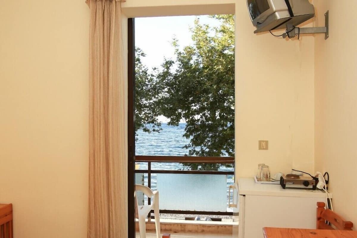 Una habitación con cama, una mesa de madera, una pequeña kitchenette y vista al mar.