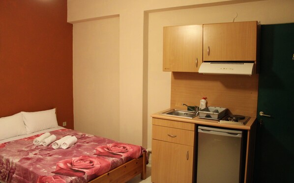 Una habitación pequeña con una cama, un armario de madera, un lavamanos y un refrigerador.