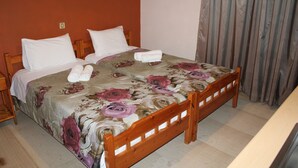 Cama doble con ropa de cama floral y dos almohadas, cabecera de madera y una cortina a la derecha.