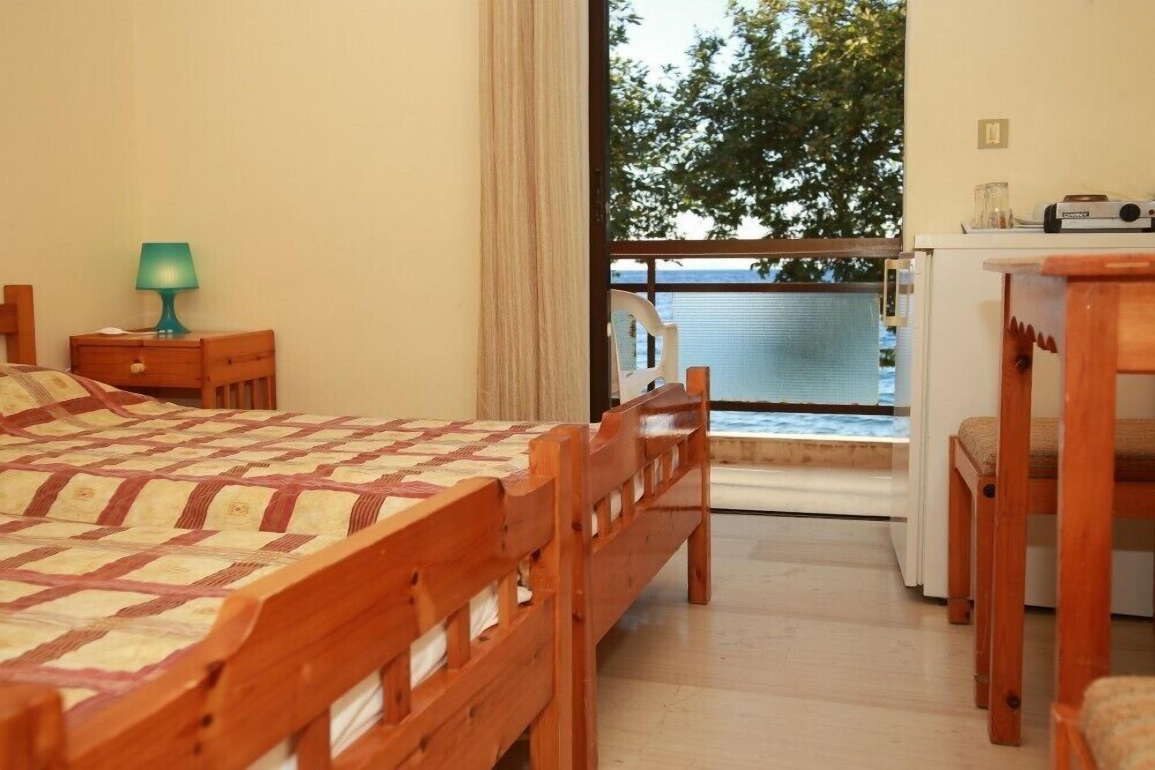 Une chambre avec un lit en bois, une petite table avec une lampe, une chaise et une vue sur la mer depuis un balcon.