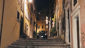 Una vista notturna di una stretta via con un'auto parcheggiata in fondo a una scalinata di pietra che conduce a un edificio.