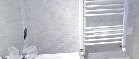 A bathroom with a white sink, a mirror, a shower with a glass door, and a towel rack.