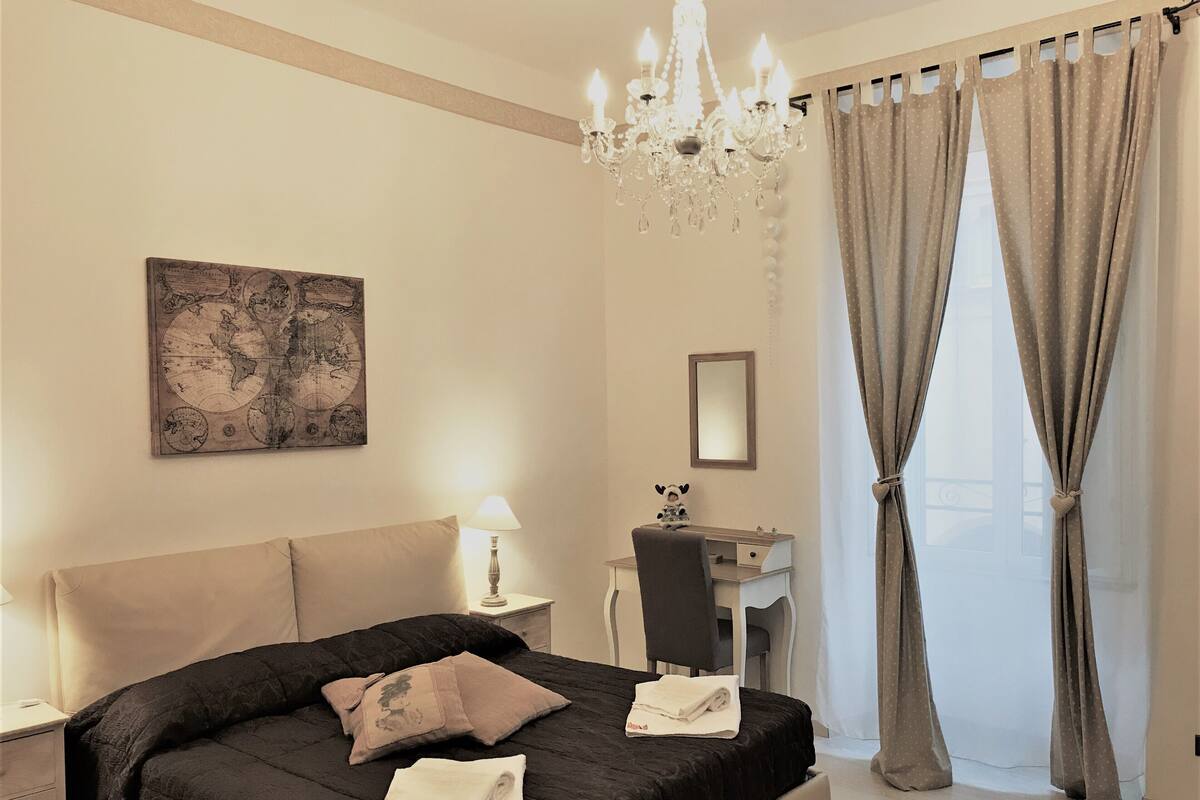 Un dormitorio con una cama grande, un escritorio, una silla, un mapa en la pared y una araña.