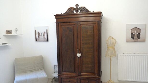 Una stanza con un'ampia armadiatura in legno, un termosifone bianco e un tavolino con una lampada.