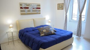 A bedroom with a large bed, two bedside tables, a lamp, a world map artwork, and a window with curtains. - Aquarius Inn (Rome)