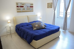 A bedroom with a large bed, two bedside tables, a lamp, a world map artwork, and a window with curtains. - Aquarius Inn (Rome)