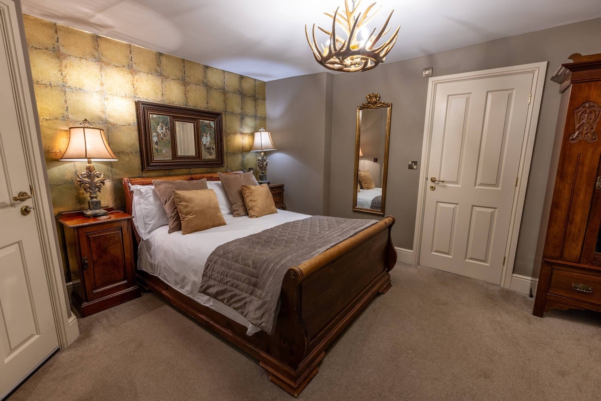 A bedroom with a large bed, two bedside tables with lamps, a mirror, a wardrobe, and a chandelier.