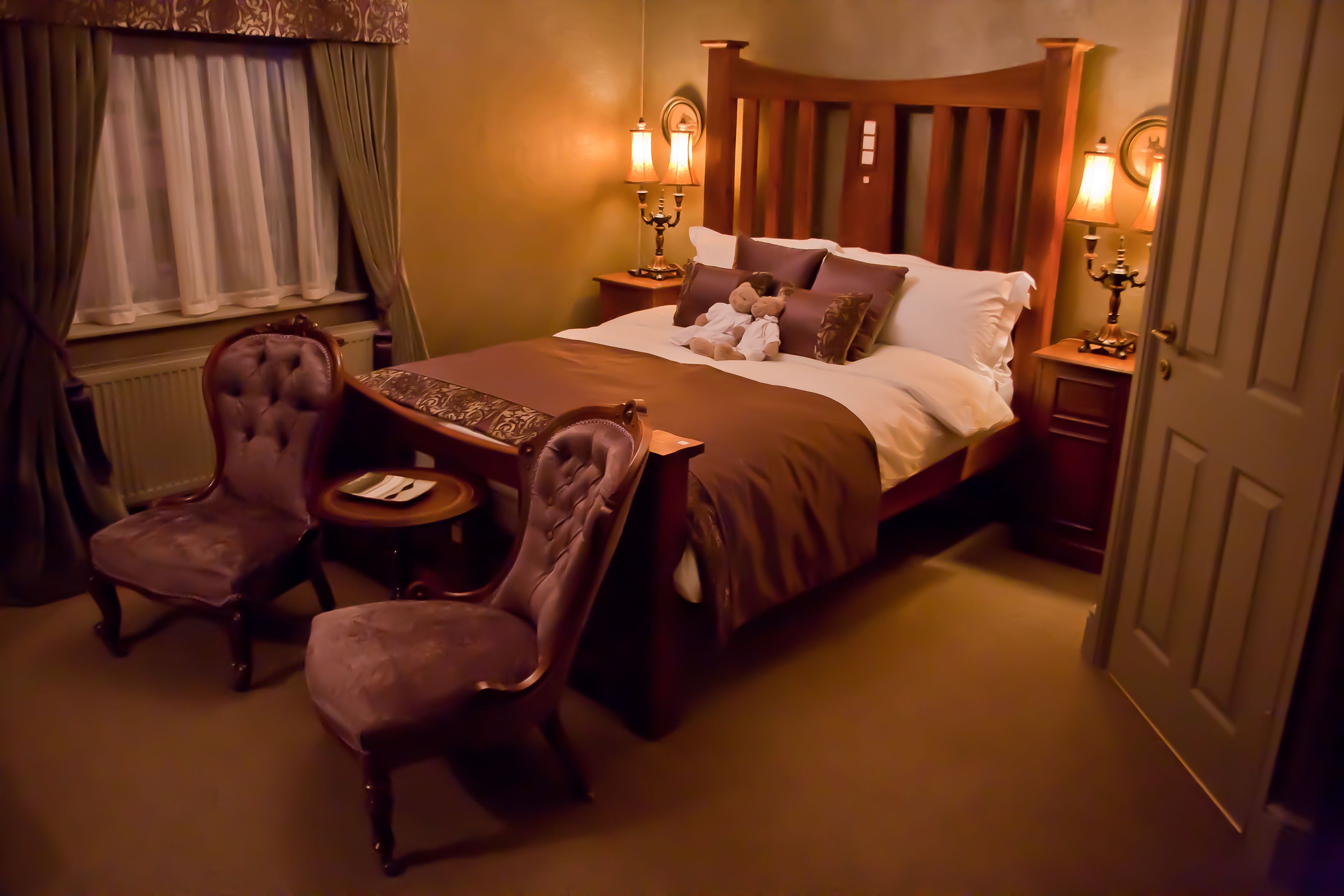 Una habitación de hotel con una cama grande, dos mesitas de noche con lámparas, una pequeña mesa redonda con una silla y una ventana con cortinas.