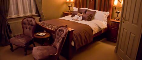 Una habitación de hotel con una cama grande, dos mesitas de noche con lámparas, una pequeña mesa redonda con una silla y una ventana con cortinas.