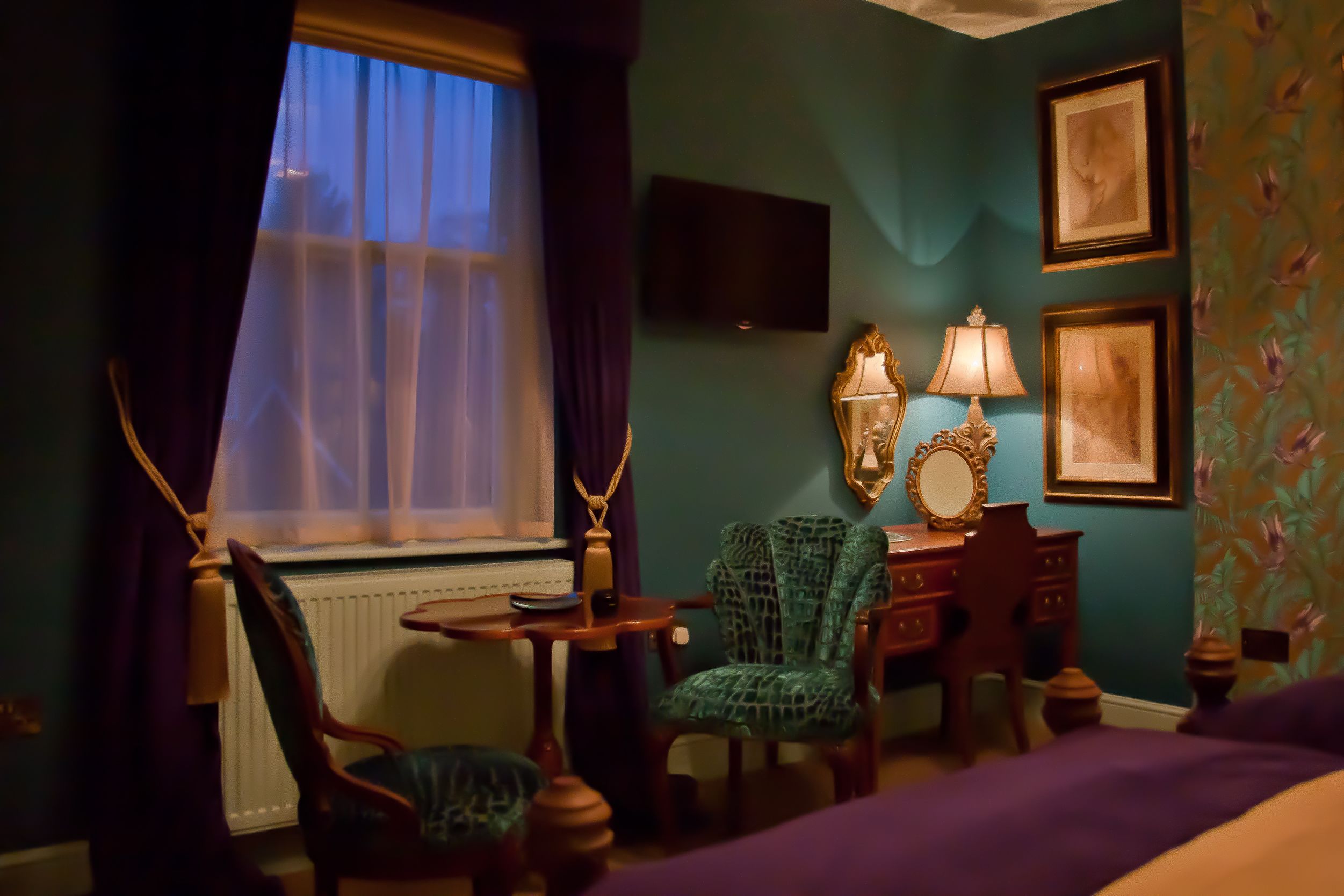 A room with a bed, a desk, a chair, a lamp, and a television on the wall.