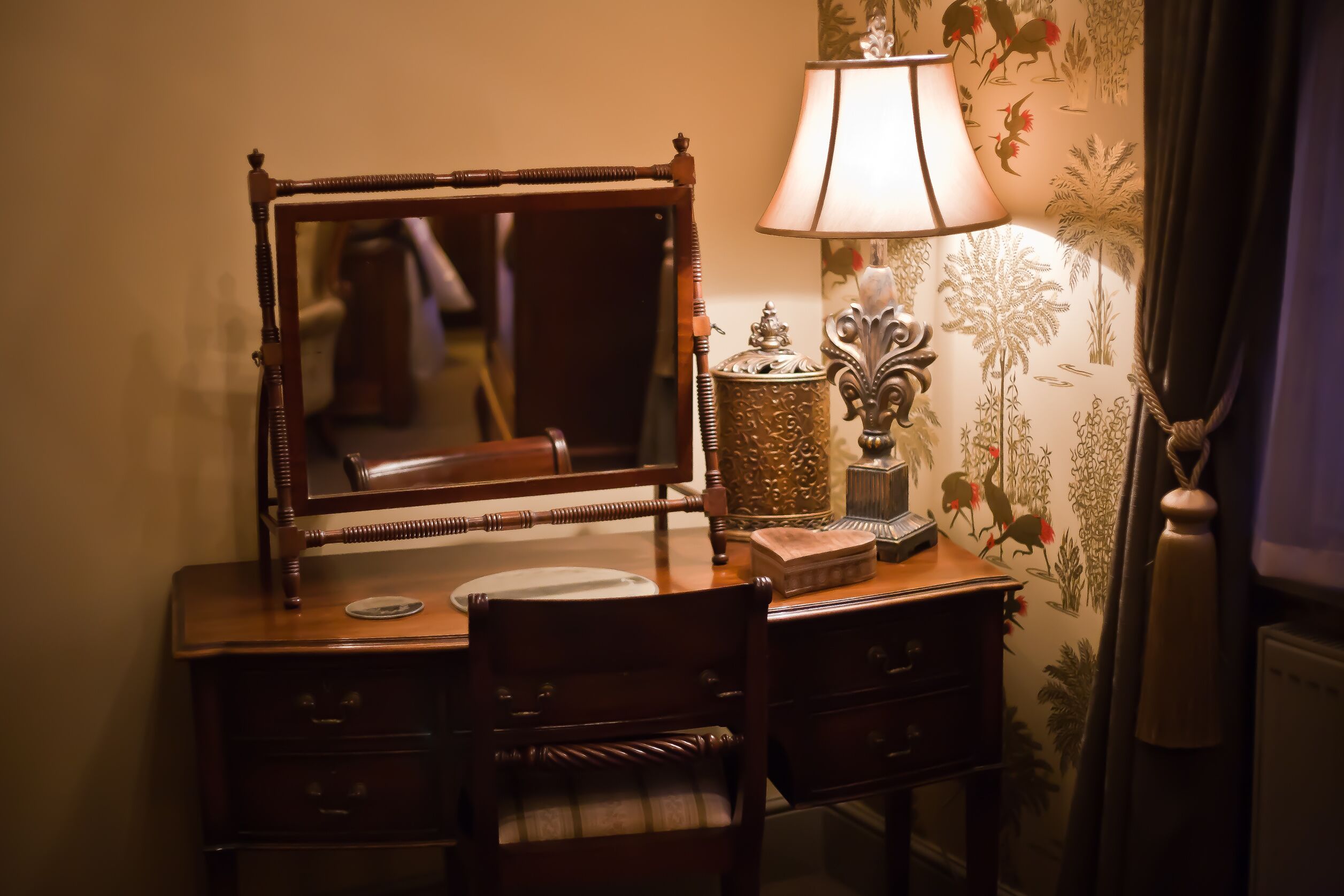 A wooden dresser with a mirror, a lamp, and a small decorative box.
