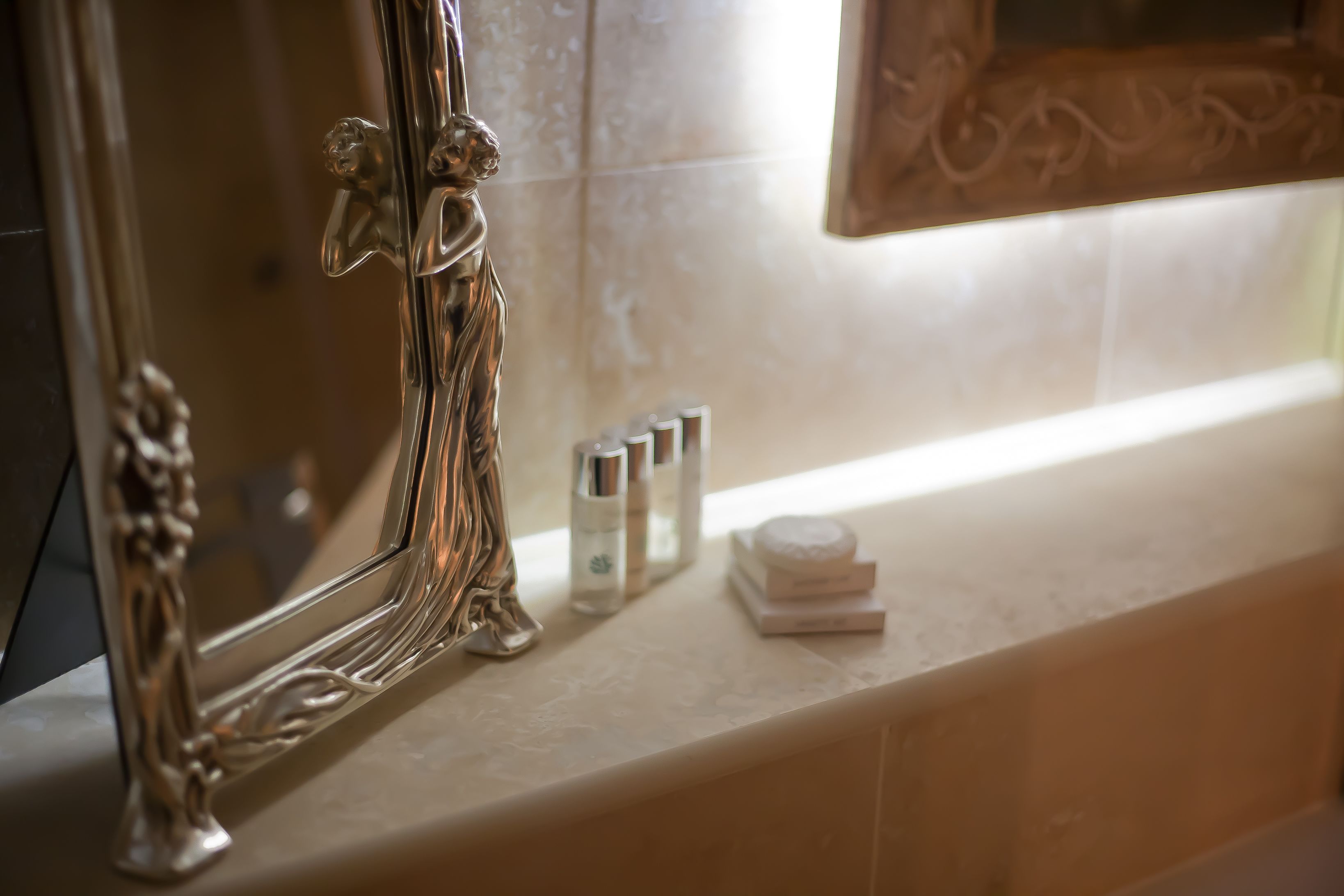 Un tocador de baño con un espejo grande, un marco plateado decorativo y artículos de aseo en la encimera.