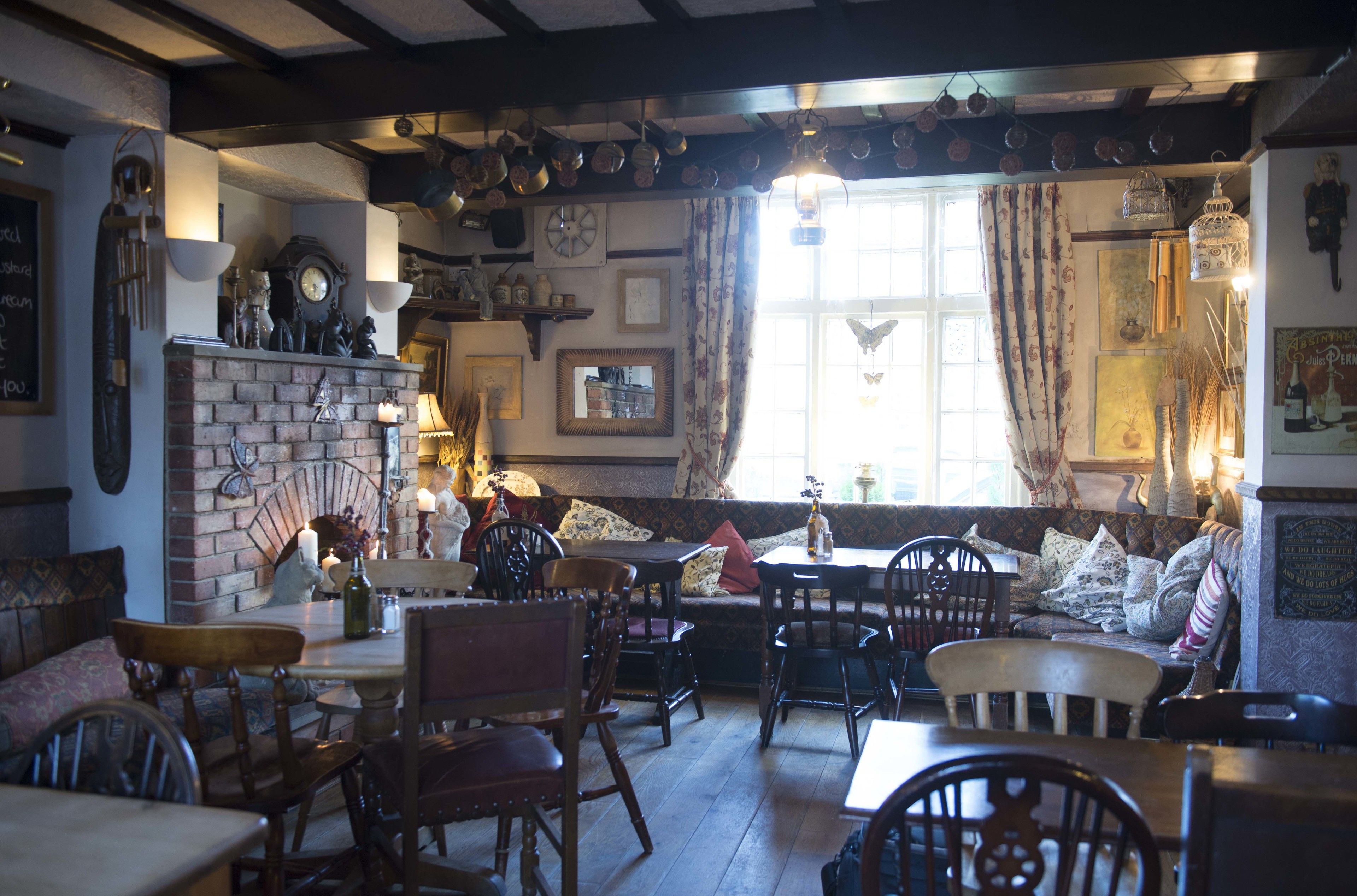 Un pub acogedor con mobiliario de madera, chimenea de ladrillo y diversas decoraciones, incluyendo un reloj y luces colgantes.